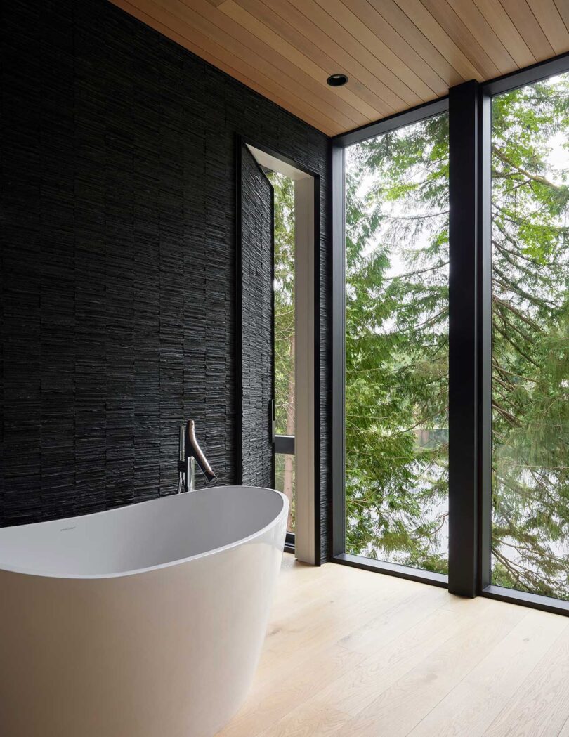 angled view of modern bathroom with black wall, windows and white tub