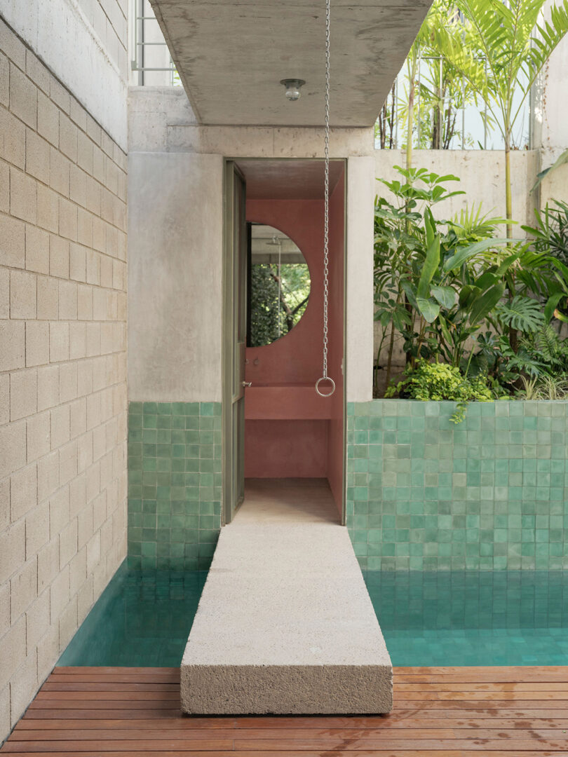 Narrow concrete bridge over a small saltwater lap pool, with half of a circular mirror and sink peeking through doorway.