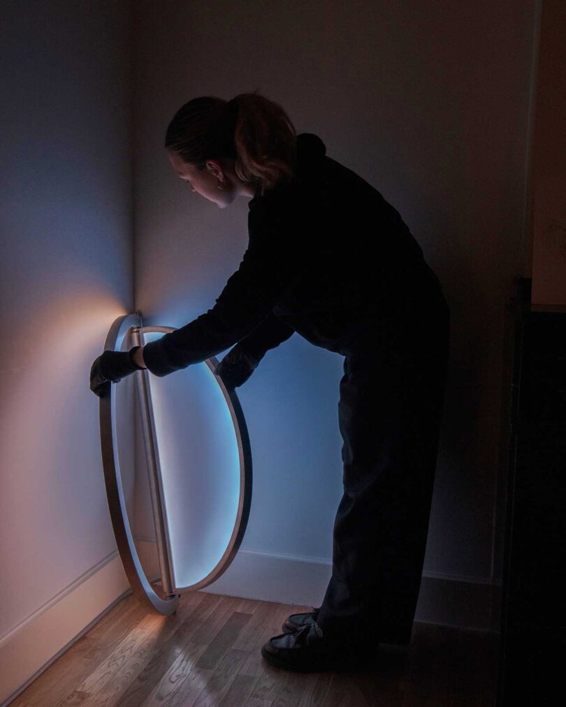 a person adjusting an oval-shaped wall light that resembles a window when illuminated
