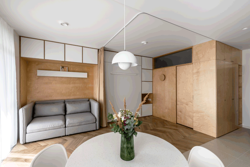 gif of angled view of small apartment with compact sofa and murphy bed next to it going up and down as a tan curtain closes to give room privacy