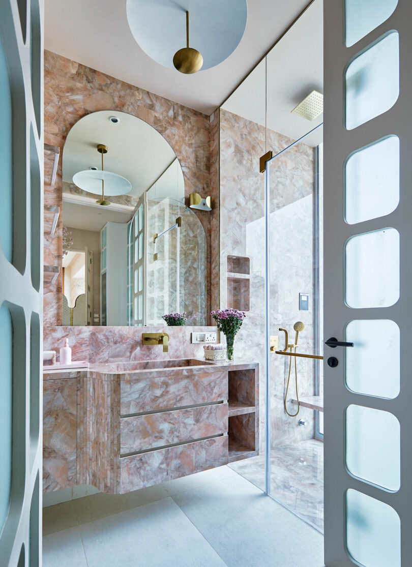 Modern bathroom with pink marble surfaces and gold accents.