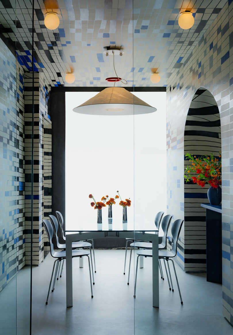 Modern dining area with blue mosaic tiles, a large pendant light, and a table set for four, featuring a large window with flowers.