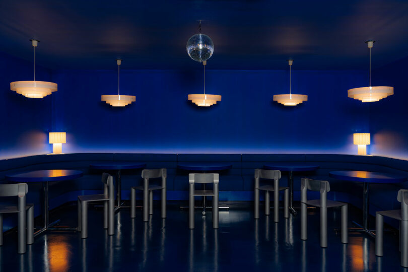 Modern bar interior with blue walls, pendant lights, bar stools, and a central disco ball, creating a calm and stylish ambiance.