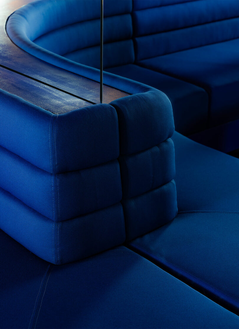 Close-up of a modern, blue tufted sofa with a sleek, minimalist design, highlighting the texture and sheen of the upholstery fabric.