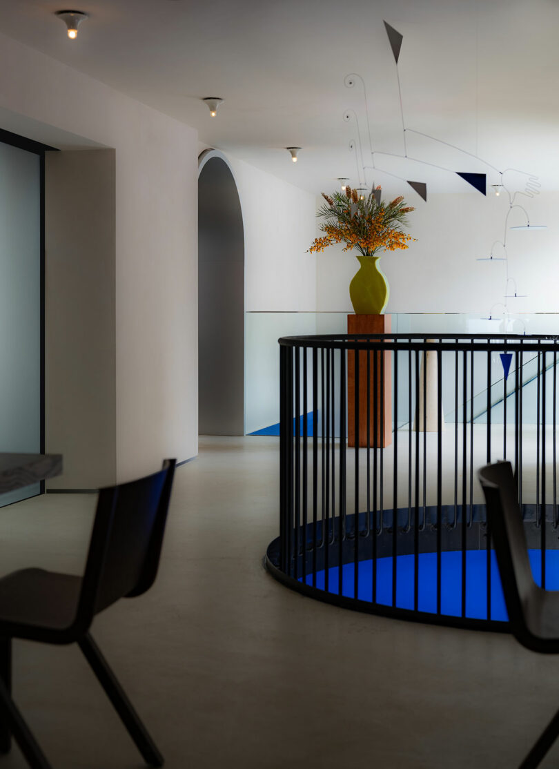 Modern interior with curved white walls, a vase of orange flowers on a blue railing, and abstract hanging lights.