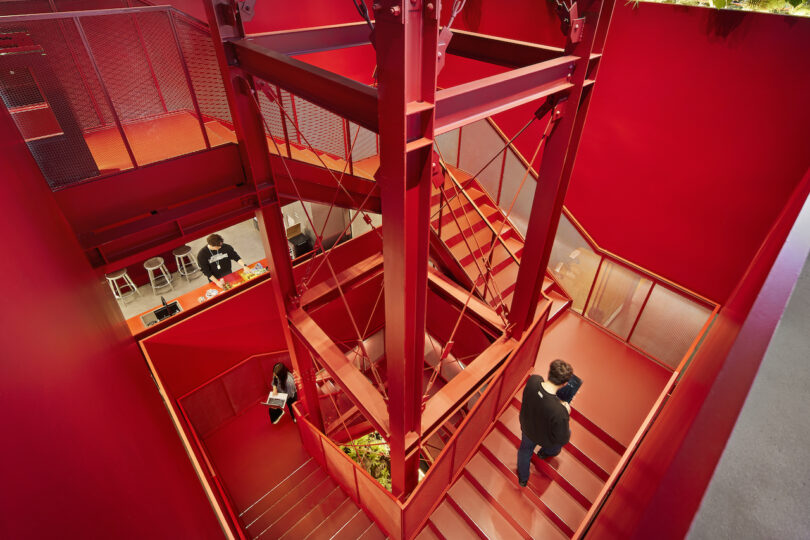 Interior view of a red multi-level staircase with people on different floors.