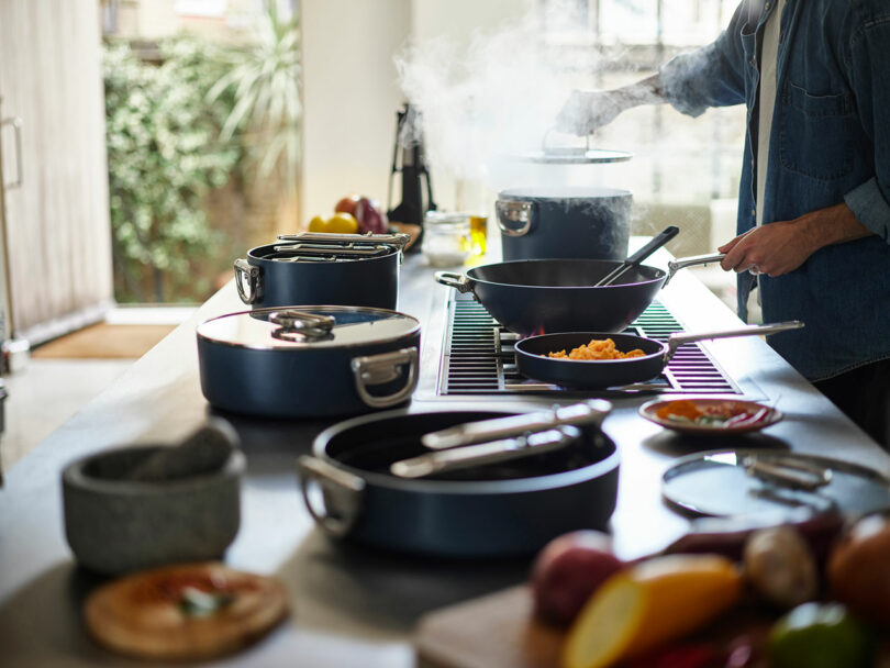 A person cooking with various pots and pans on a kitchen stove.