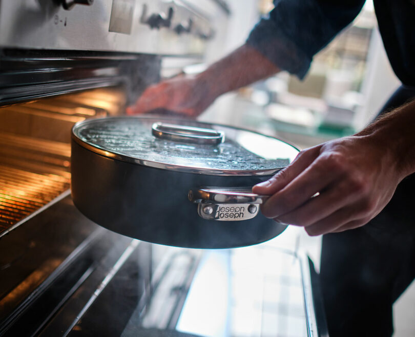 A person sliding a round, glass-lidded casserole dish into an oven.