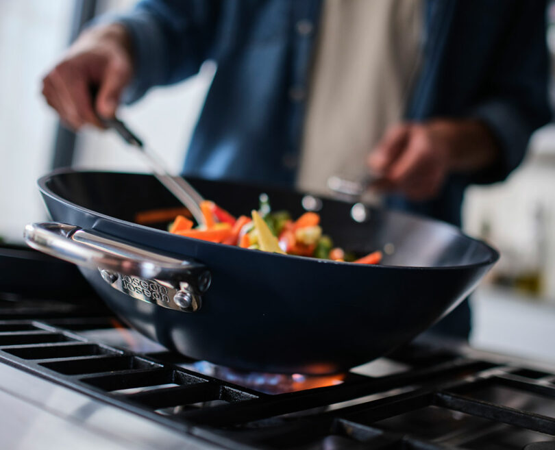 A person sautéing vegetables in a wok on a stove.