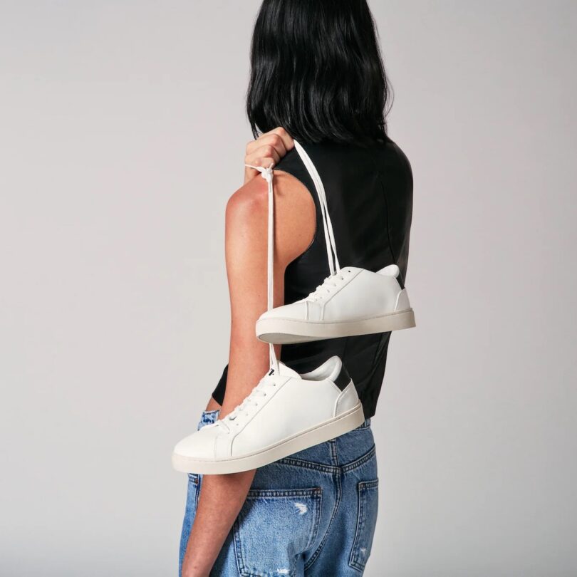 woman turned around holding white sneakers by its laces and slung over her shoulder