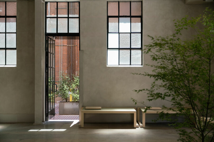 Serene indoor space with natural light, a wooden bench, and a view of an outdoor patio through large windows.