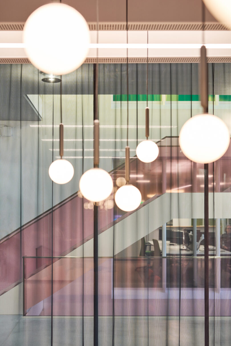 Modern interior with round pendant lights and glass partitions overlooking a staircase.